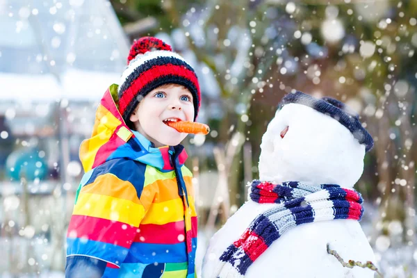 Garoto engraçado em roupas coloridas fazendo um boneco de neve, ao ar livre — Fotografia de Stock