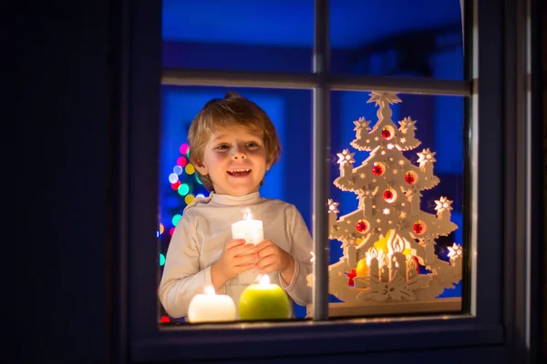 Μικρό αγόρι παιδί στέκεται από παράθυρο στο χρόνο Χριστουγέννων και κρατώντας — Φωτογραφία Αρχείου