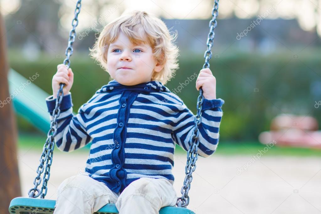 Adorable toddler boy having fun chain swing on outdoor playgroun