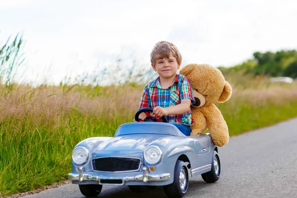 Liten unge pojke köra stor leksaksbil med en björn, utomhus. — Stockfoto