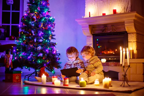 Två små barn sitter vid öppna spisen hemma på jul — Stockfoto