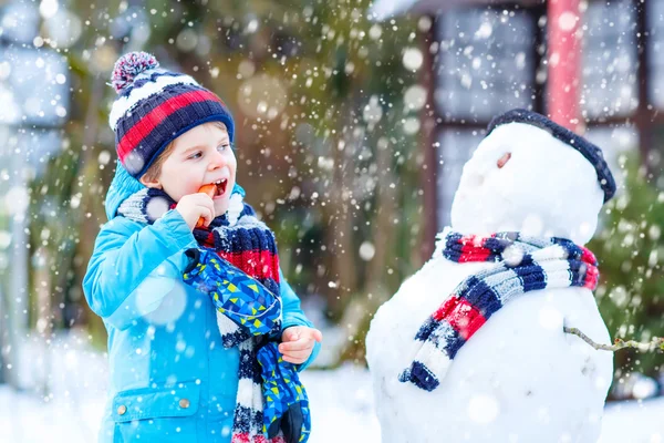 Lustige Junge in bunten Kleidern, die einen Schneemann, im Freien — Stockfoto