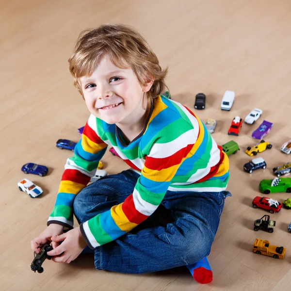 Lille blond barn leger med masser af legetøjsbiler indendørs - Stock-foto