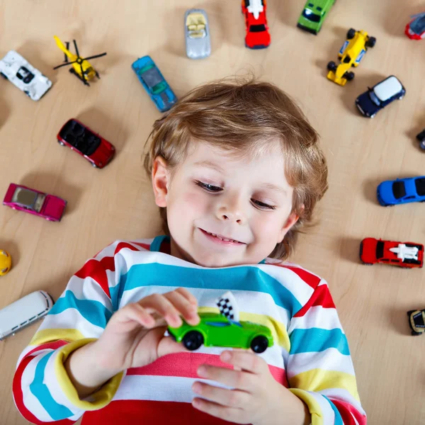 Pequeño niño rubio jugando con un montón de coches de juguete en interiores —  Fotos de Stock