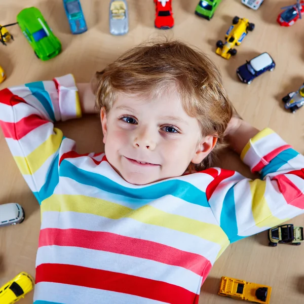 Pequeño niño rubio jugando con un montón de coches de juguete en interiores —  Fotos de Stock