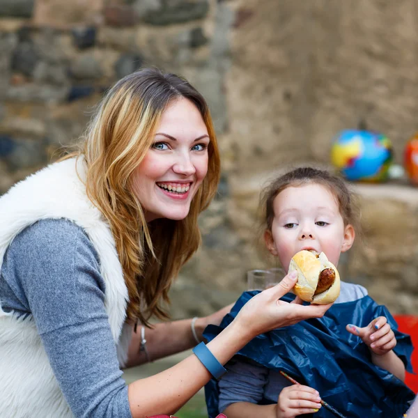 Mother feeding little kid girl with hot dog outdoors — Stockfoto