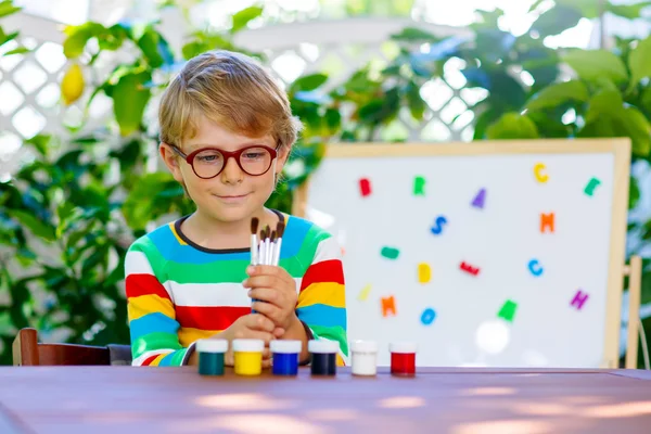 Kleiner Schuljunge mit Brille, der viele Pinsel und c hält — Stockfoto
