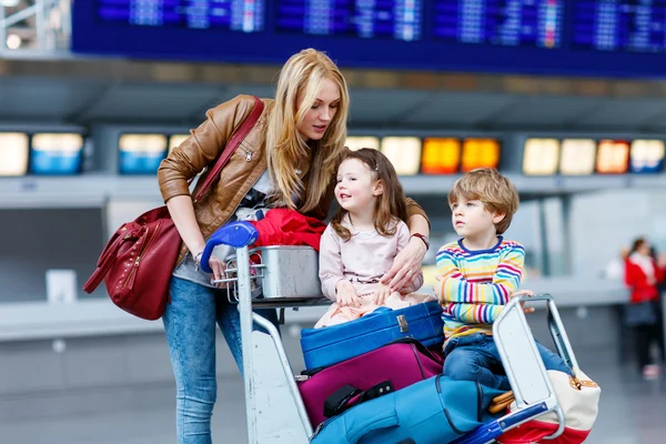 Little girl and boy and young mother with suitcases on airport — Stock Photo, Image