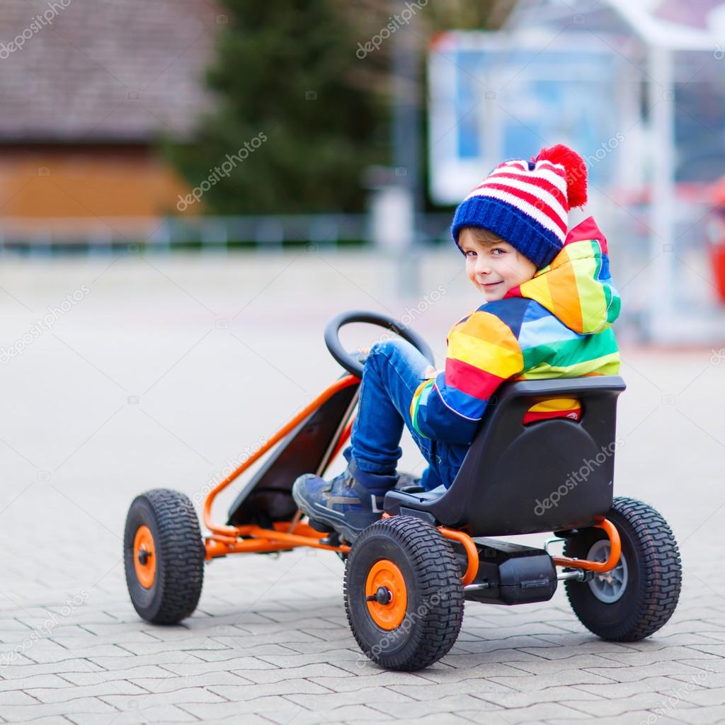Little kid boy having fun on toy race car outdoors