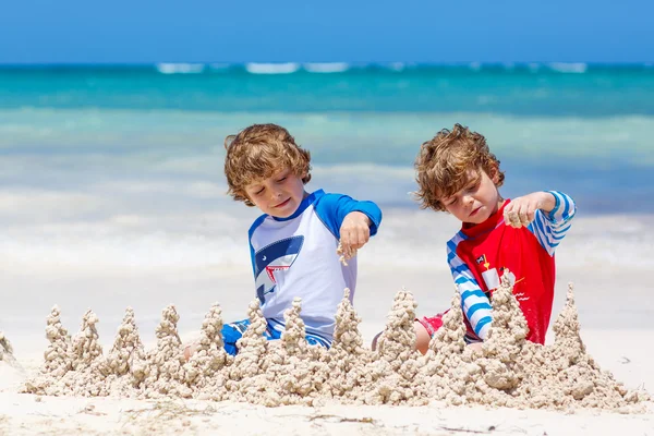 Due bambini ragazzi che costruiscono castello di sabbia sulla spiaggia tropicale — Foto Stock