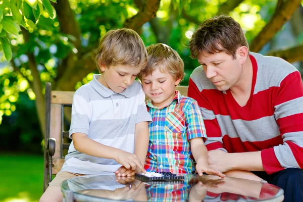 Two little kid boys and father playing together checkers game — Stock Photo, Image