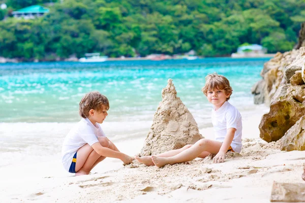 Due bambini ragazzi che costruiscono castello di sabbia sulla spiaggia tropicale — Foto Stock