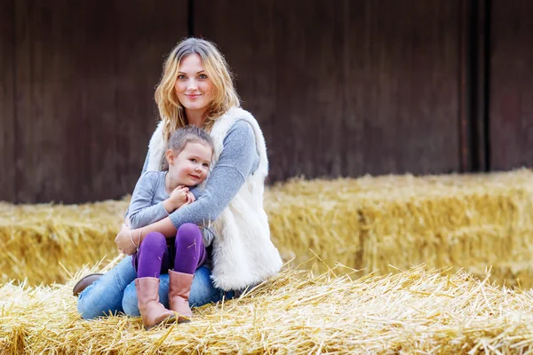 Menina feliz e mãe se divertindo com feno em uma fazenda — Fotografia de Stock