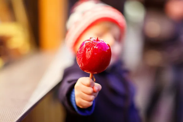 Niño pequeño comiendo manzana cristalizada en el mercado de Navidad —  Fotos de Stock
