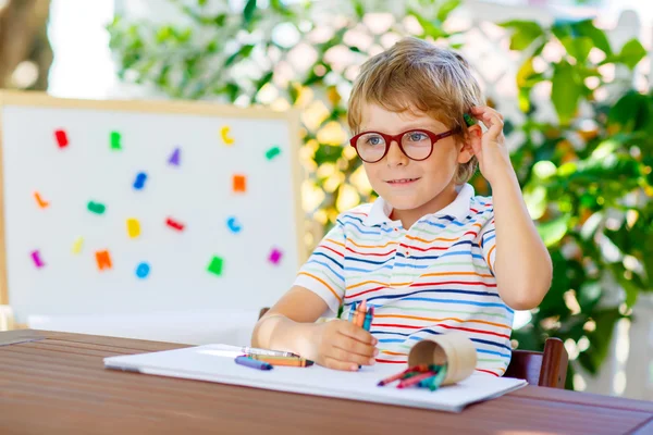Маленький школяр хлопчик в окулярах тримає воскові олівці — стокове фото