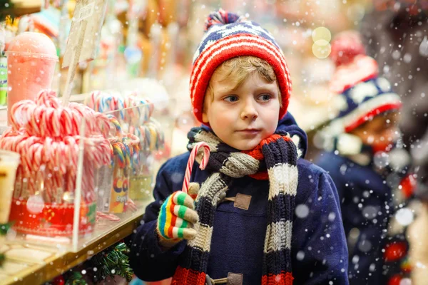 Little kid boy with candy cane stand on Christmas market — Stock Photo, Image