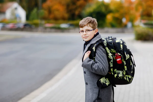 Gelukkige jongen met bril en rugzak of tas. Schoolkind in stijlvolle fashon coan op weg naar de middelbare of middelbare school op koude herfstdag. Gezond kind buiten op straat, op regenachtige dag. — Stockfoto