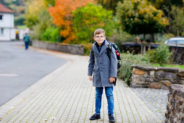 Rapaz feliz com óculos e mochila ou mochila. Schoolkid em elegante casulo fashon a caminho do ensino médio ou médio no dia frio de outono. Criança saudável ao ar livre na rua, no dia chuvoso. — Fotografia de Stock