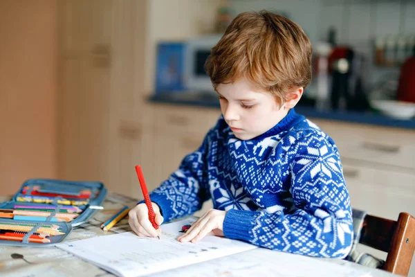 Одинокий школьник дома делает домашнее задание. Маленький ребенок пишет красочными карандашами в помещении. Начальная школа и образование. Домашнее обучение во время пандемии коронного вируса — стоковое фото