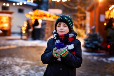Küçük şirin çocuk Alman Noel pazarında sıcak çocuk kokteyli ya da çikolata içiyor. Almanya 'nın geleneksel aile pazarında mutlu bir çocuk renkli kışlık giysiler içinde gülen bir çocuk.