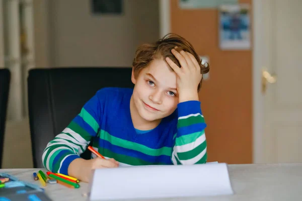 Portrét roztomilého, šťastného školáka, jak doma dělá domácí úkoly. Malé dítě píše barevnými tužkami, uvnitř. Základní škola a vzdělání. Děcko se učí psát písmena a čísla — Stock fotografie