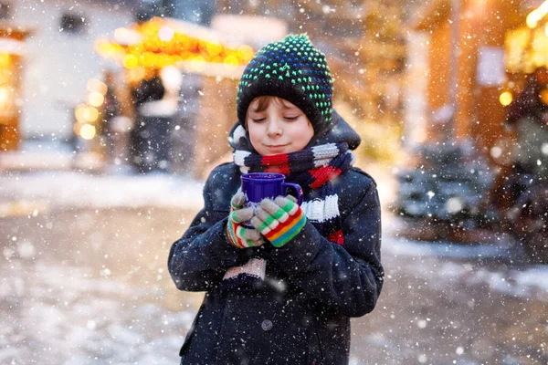 작고 귀여운 남자 애가 독일 크리스마스 마켓에서 펀치나 초콜릿을 마시고 있어. 화려 한 겨울 옷을 입은 웃는 소년, 독일의 전통 가정 시장에서 행복 한 어린이 — 스톡 사진