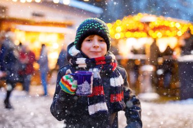 Küçük şirin çocuk Alman Noel pazarında sıcak çocuk kokteyli ya da çikolata içiyor. Almanya 'nın geleneksel aile pazarında mutlu bir çocuk renkli kışlık giysiler içinde gülen bir çocuk.