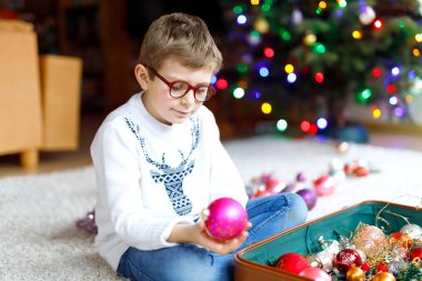 Gözlüklü, renkli eski yılbaşı oyuncakları ve eski bavulunda topları olan güzel bir çocuk. Çocuk Noel ağacı süslemesi