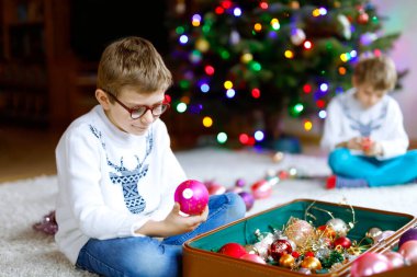 Gözlüklü, renkli eski yılbaşı oyuncakları ve eski bavulunda topları olan güzel bir çocuk. Çocuklar Noel ağacı süslüyorlar