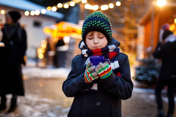 ドイツのクリスマスマーケットで熱い子供のパンチやチョコレートを飲む小さなかわいい子供の男の子。ドイツの伝統的な家庭市場で幸せな子供、カラフルな冬の服で笑う男の子 — ストック写真