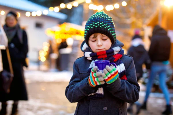 Küçük şirin çocuk Alman Noel pazarında sıcak çocuk kokteyli ya da çikolata içiyor. Almanya 'nın geleneksel aile pazarında mutlu bir çocuk renkli kışlık giysiler içinde gülen bir çocuk. — Stok fotoğraf