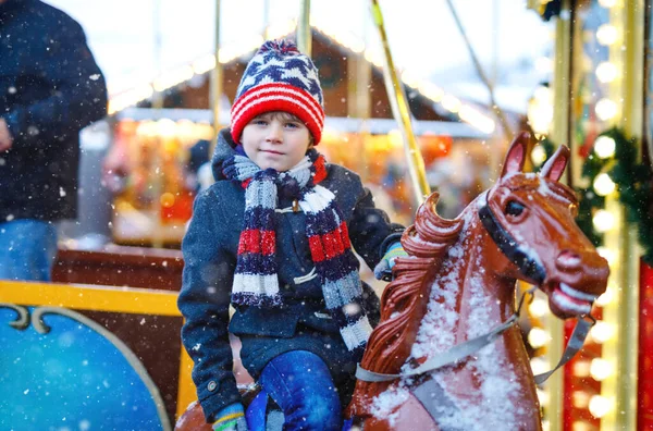 Adorabile ragazzino che cavalca su un allegro cavallino giostra al luna park o al mercatino di Natale, all'aperto. Bambino felice divertirsi sul tradizionale mercato di Natale in famiglia in Germania — Foto Stock