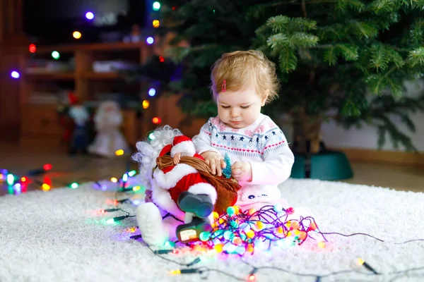 Αξιολάτρευτο κοριτσάκι κρατώντας πολύχρωμα φώτα γιρλάντα σε χαριτωμένα χέρια. Μικρό παιδί με γιορτινή ενδυμασία στολίζοντας χριστουγεννιάτικο δέντρο με οικογένεια. Πρώτη γιορτή των παραδοσιακών διακοπών που ονομάζεται Weihnachten — Φωτογραφία Αρχείου