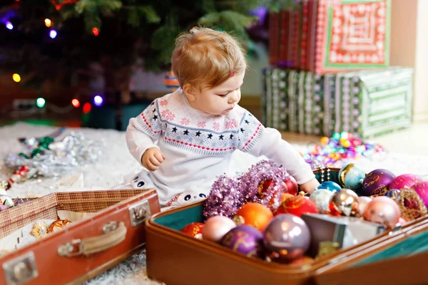 Adorable baby girl holding colorful lights garland in cute hands. Little child in festive clothes decorating Christmas tree with family. First celebration of traditional holiday called Weihnachten — Stock Photo, Image