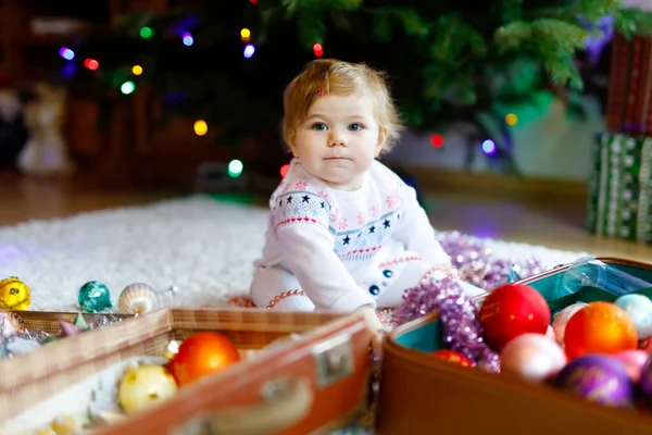 Schattige baby meisje met kleurrijke lichten bloemenslinger in schattige handen. Klein kind in feestelijke kleding versieren kerstboom met familie. Eerste viering van de traditionele feestdag genaamd Weihnachten — Stockfoto