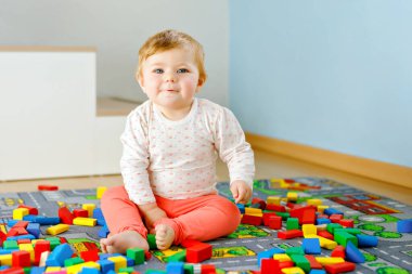 Eğitici oyuncaklarla oynayan sevimli bir kız bebek. Mutlu sağlıklı bir çocuk, evdeki renkli tahta bloklarla eğleniyor. Bebek öğrenme renkleri ve biçimleri