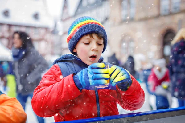 Glad liten pojke i färgglada varma kläder på skridskobana av julmarknad eller rättvis dricka varm punch eller choklad. Friska barn som har roligt på skridskor. personer som har aktiv vinterfritid — Stockfoto