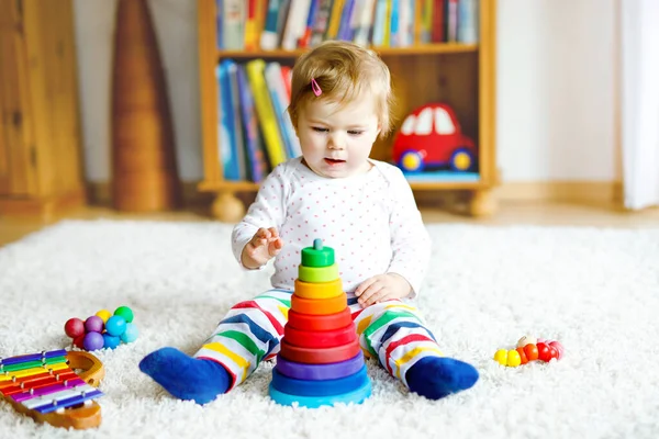 Adorable linda y hermosa niña jugando con juguetes educativos en casa o en la guardería. Feliz niño sano que se divierte con colorida pirámide de juguete Rainboy de madera. Niño aprendiendo diferentes habilidades — Foto de Stock