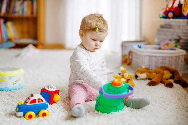 Šťastná radostná holčička hrající si s různými barevnými hračkami doma. Rozkošné zdravé batole dítě baví hrát sám. Aktivní volný čas v interiéru, školce nebo divadelní škole. — Stock fotografie