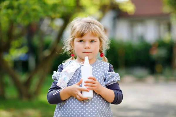 Kleine peuter meisje met medisch masker als bescherming tegen pandemische coronavirus quarantaine ziekte. Schattig kinder flesje met ontsmettingsmiddel voor het reinigen van handen. beschermende uitrusting tegen covid — Stockfoto