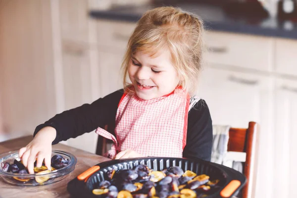 Carina la bambina che cuoce la torta di prugne a casa. Buon bambino sorridente che aiuta e prepara prugne per torta in cucina domestica. Cibo sano fatto in casa. — Foto Stock