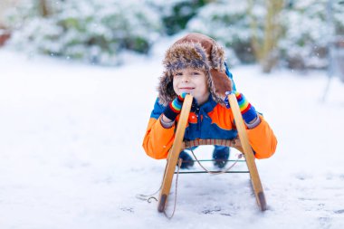 Küçük çocuk kışın kızakla geziyor.
