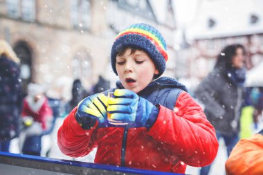 Noel pazarında kayak pistinde renkli, sıcak kokteyl ya da çikolata içen küçük çocuk. Sağlıklı bir çocuk buz pateninde eğleniyor. Aktif kış tatili yapan insanlar