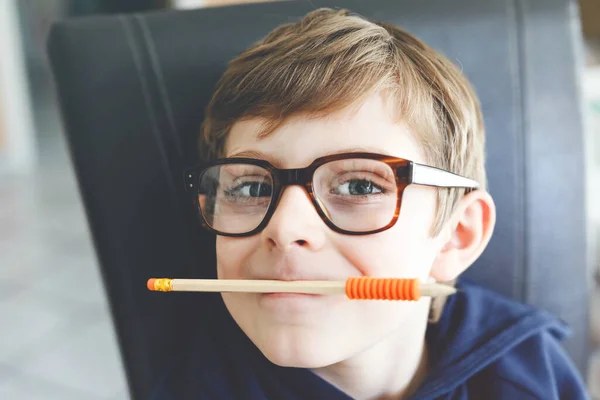 Ritratto di un ragazzino carino con gli occhiali. Bella bambina felice che guarda la macchina fotografica. Schoolboy prendere in giro con una penna, tenendo in bocca e dietro l'orecchio. Concetto educativo. — Foto Stock