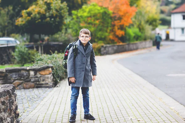 Szczęśliwy chłopiec w okularach i plecaku albo torbie. Uczennica w stylowym fashon coan w drodze do gimnazjum lub liceum w zimny jesienny dzień. Zdrowe dziecko na ulicy, w deszczowe dni. — Zdjęcie stockowe