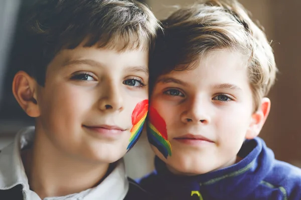 Dwóch chłopców z malowaną tęczą i kolorowymi kolorami twarzy podczas pandemicznej kwarantanny koronawirusowej. Dzieci robią i malują tęcze na całym świecie. Rodzeństwo, najlepsi przyjaciele. — Zdjęcie stockowe
