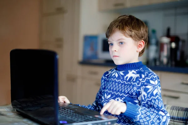 Одинокий мальчик учится дома на ноутбуке для школы. Очаровательный ребенок делает домашнее задание и с помощью ноутбука и современных гаджетов. Концепция домашнего обучения во время карантина пандемического вируса короны — стоковое фото