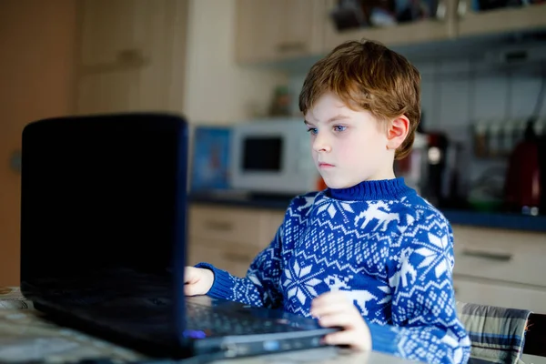 Niño solitario aprendiendo en casa en el portátil para la escuela. Niño adorable haciendo la tarea y el uso de cuaderno y aparatos modernos. Concepto de educación en el hogar durante la cuarentena de bloqueo del virus corona pandémica —  Fotos de Stock