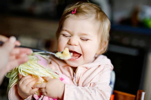 スプーンマッシュ野菜とピューレから食べる愛らしい赤ちゃんの女の子。食べ物、子供、食事、人の概念-かわいい幼児、椅子に座って家で食べるスプーンを持つ娘. — ストック写真