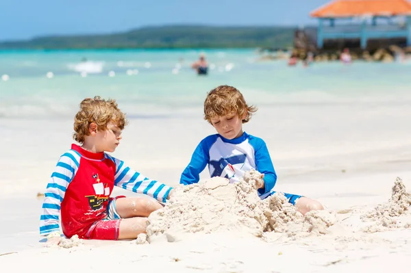 Twee kleine jongens die plezier hebben met het bouwen van een zandkasteel op het tropische strand van carribean eiland. — Stockfoto